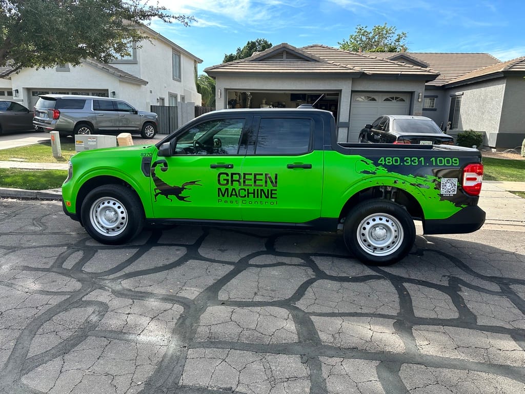 Bright green pest-control truck with GREEN MACHINE logo parked on a residential street with houses in the background on a sunny day.
