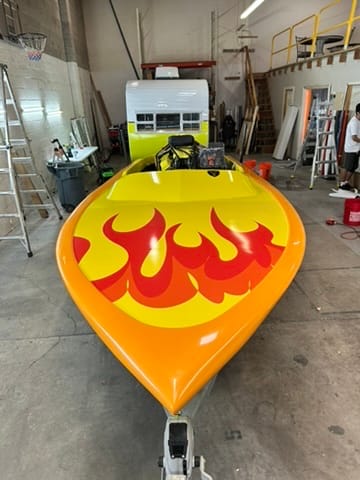 Bright yellow speedboat with red flame graphics, inside a workshop on a trailer. (front view)