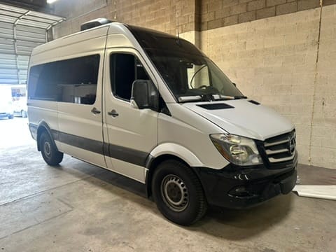 White Mercedes-Benz Sprinter cargo van parked inside a concrete-walled workshop/garage, front-right view.