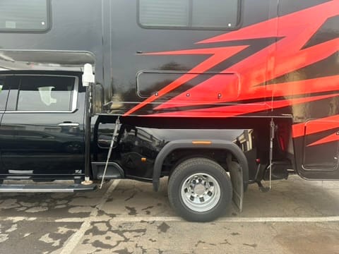 Side view of a black motorhome with bold red graphics, showing the wheel, fender, and entry area near the cab.