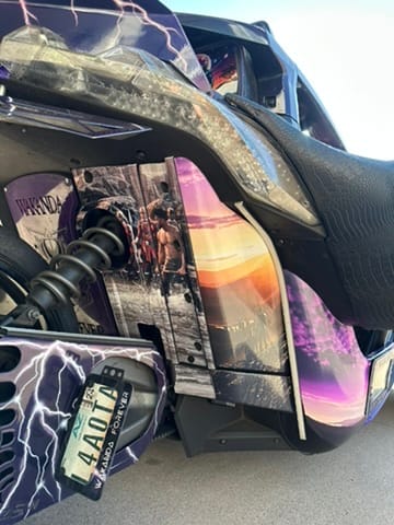 Close-up of a customized motorcycle with purple lightning graphics, a framed poster on the side, and a visible license plate.