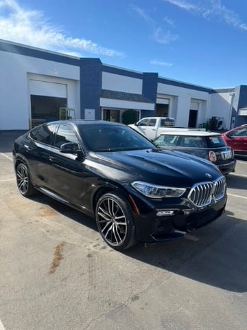 Black BMW SUV with large alloy wheels parked outside a blue-and-white industrial building on a sunny day in a paved lot.