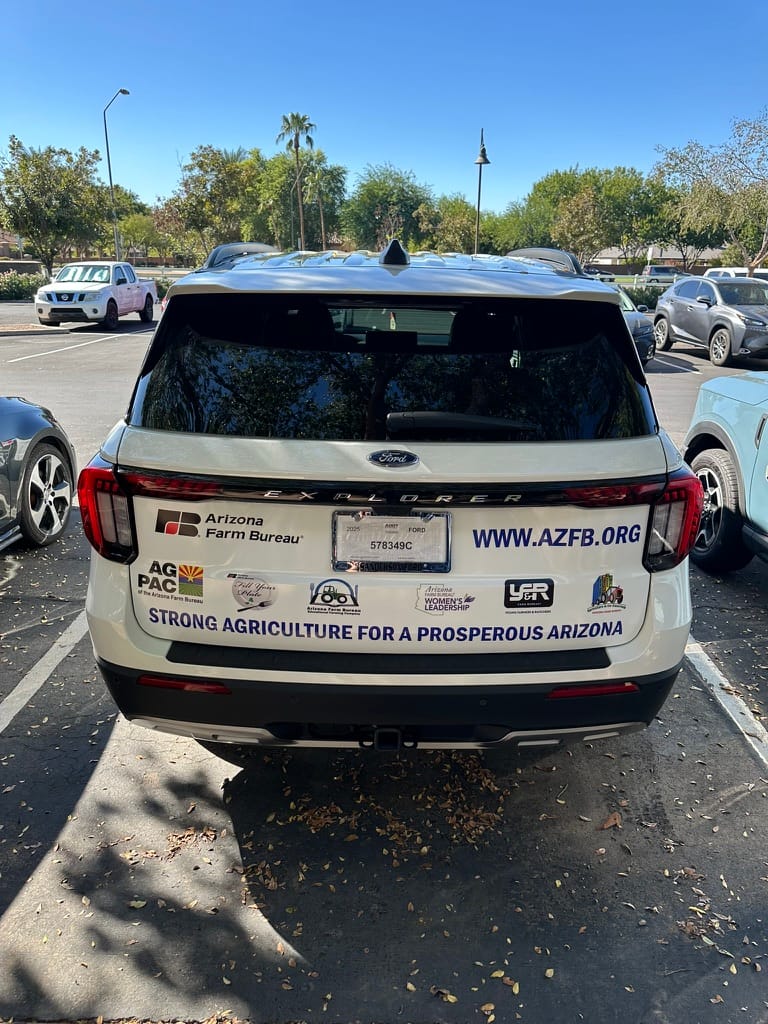Rear view of a white Ford Explorer in a parking lot with bumper stickers promoting the Arizona Farm Bureau and 'Strong Agriculture for a Prosperous Arizona'