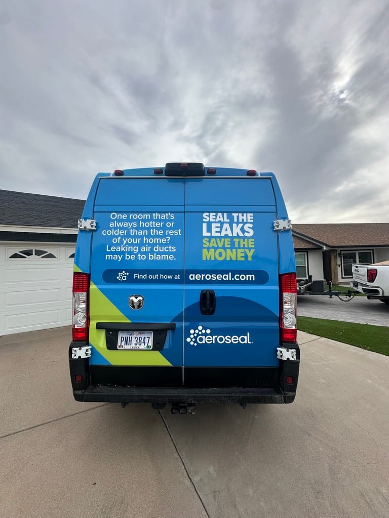Rear of a blue AeroSeal van with bold yellow and white text announcing 'Seal the leaks, save the money' in a driveway.