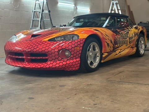Custom flame-painted orange convertible sports car with honeycomb front and honey decals in a garage workshop