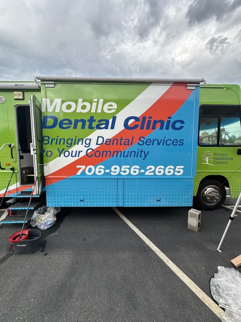 Mobile dental clinic van with colorful graphics and the phone number 706-956-2665.