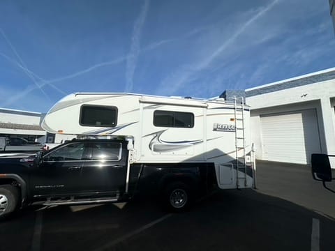 Black pickup truck pulling a large white fifth-wheel camper parked in front of a building with garage doors of a commercial facility.