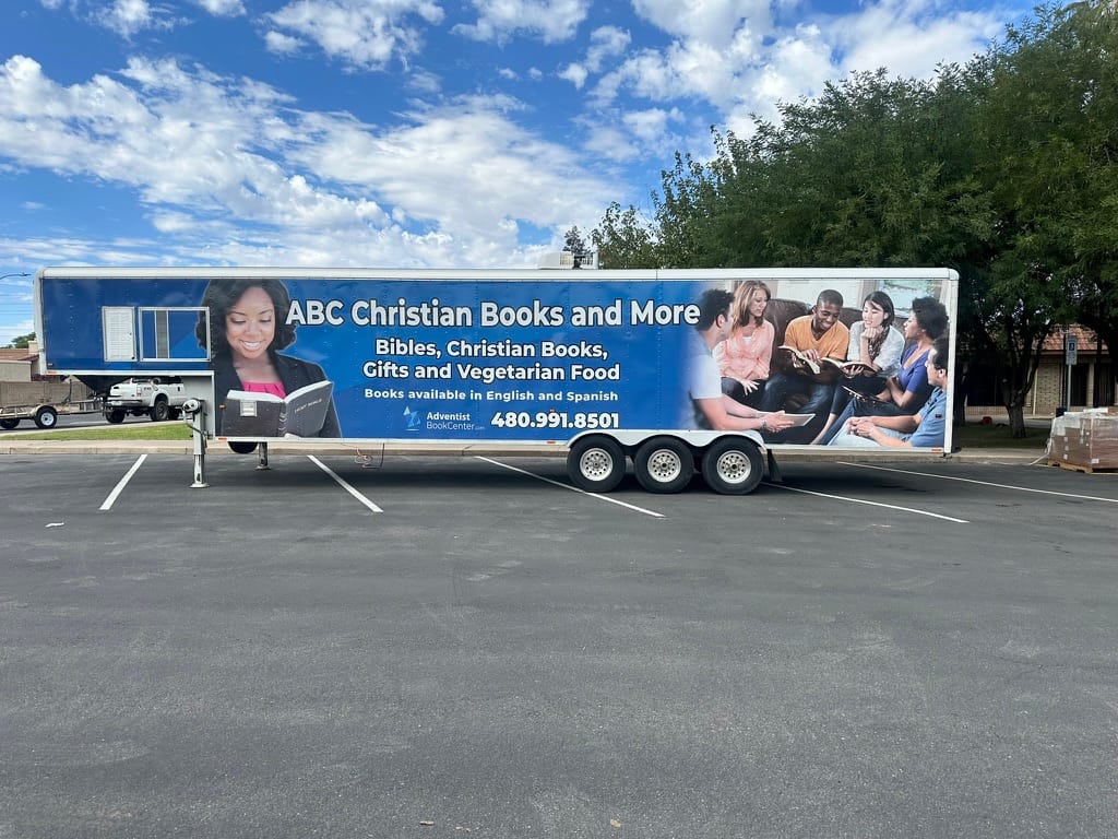 Blue advertisement trailer for ABC Christian Books and More with people reading and smiling, parked in a lot under a partly cloudy sky.